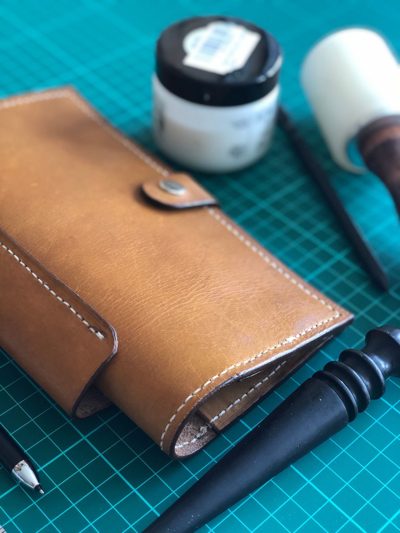 A leather wallet and hand tools on a cutting mat