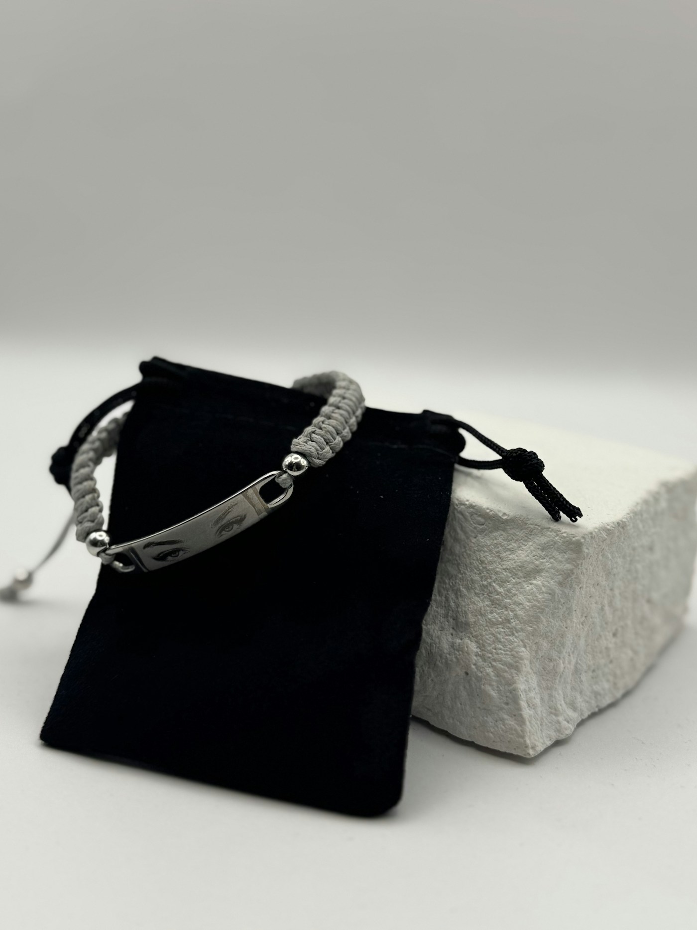 Gray braided bracelet with an engraved metal plate on a black pouch