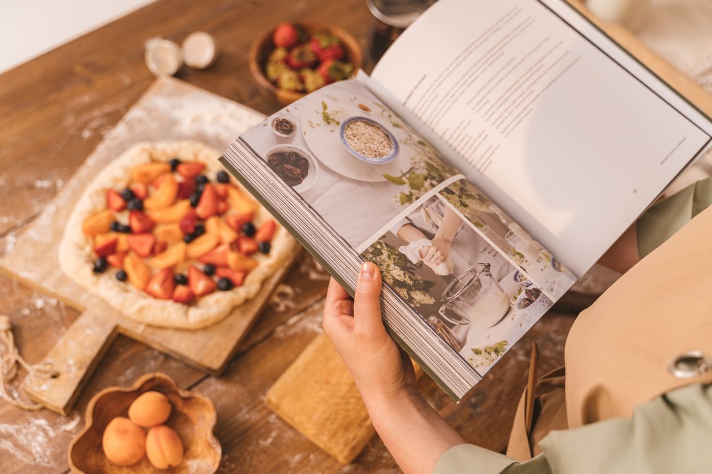 Open recipe book beside a fruit tart and baking ingredients