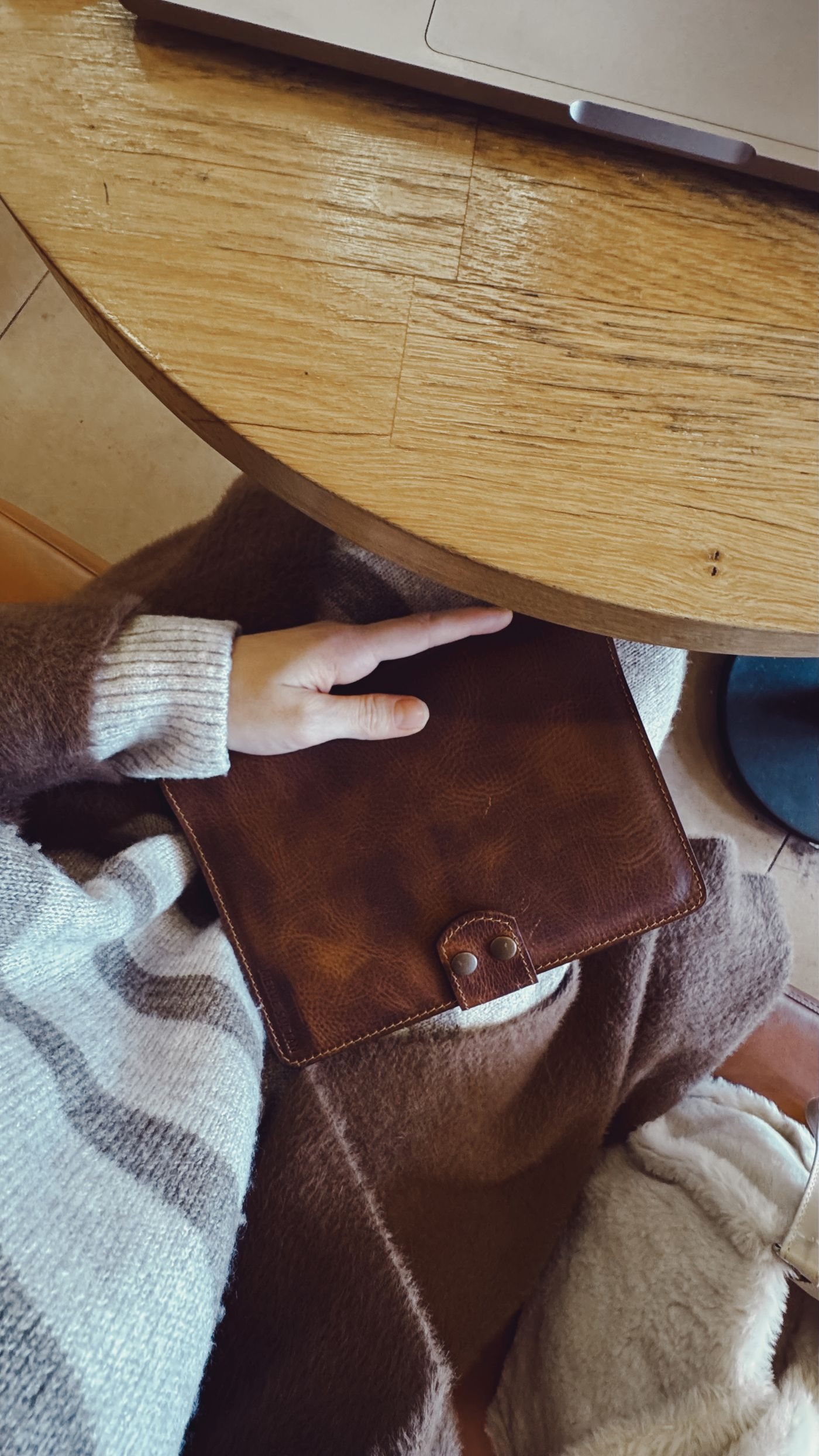 A leather notebook held beside a laptop on a wooden table